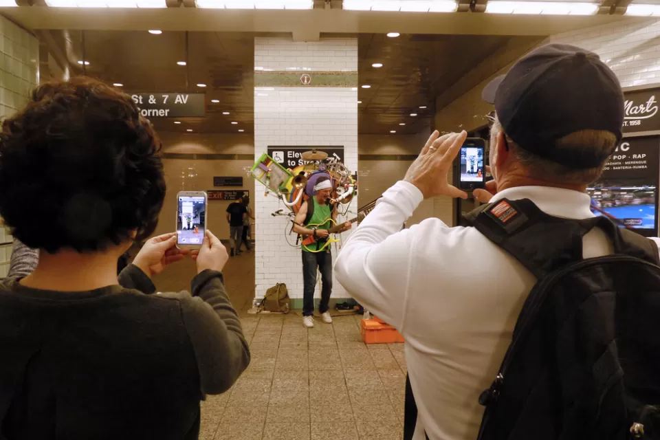 A performer holding numerous instruments plays for a crowd in the New York Subway.